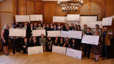students hold up large checks as they pose for a photo following the business plan competition