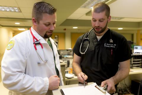 two men in medical garb review paper on a clipboard