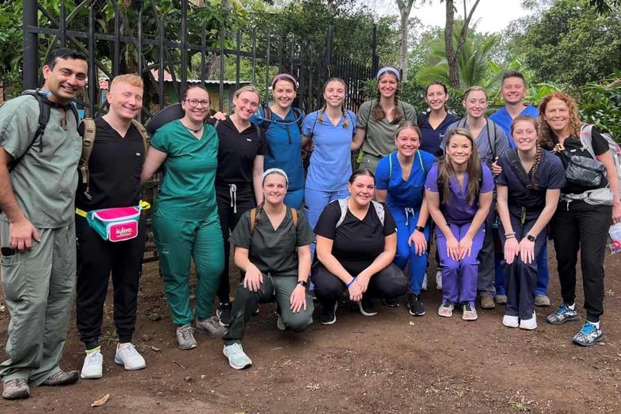 A group of students in medical scrubs pose outdoors.