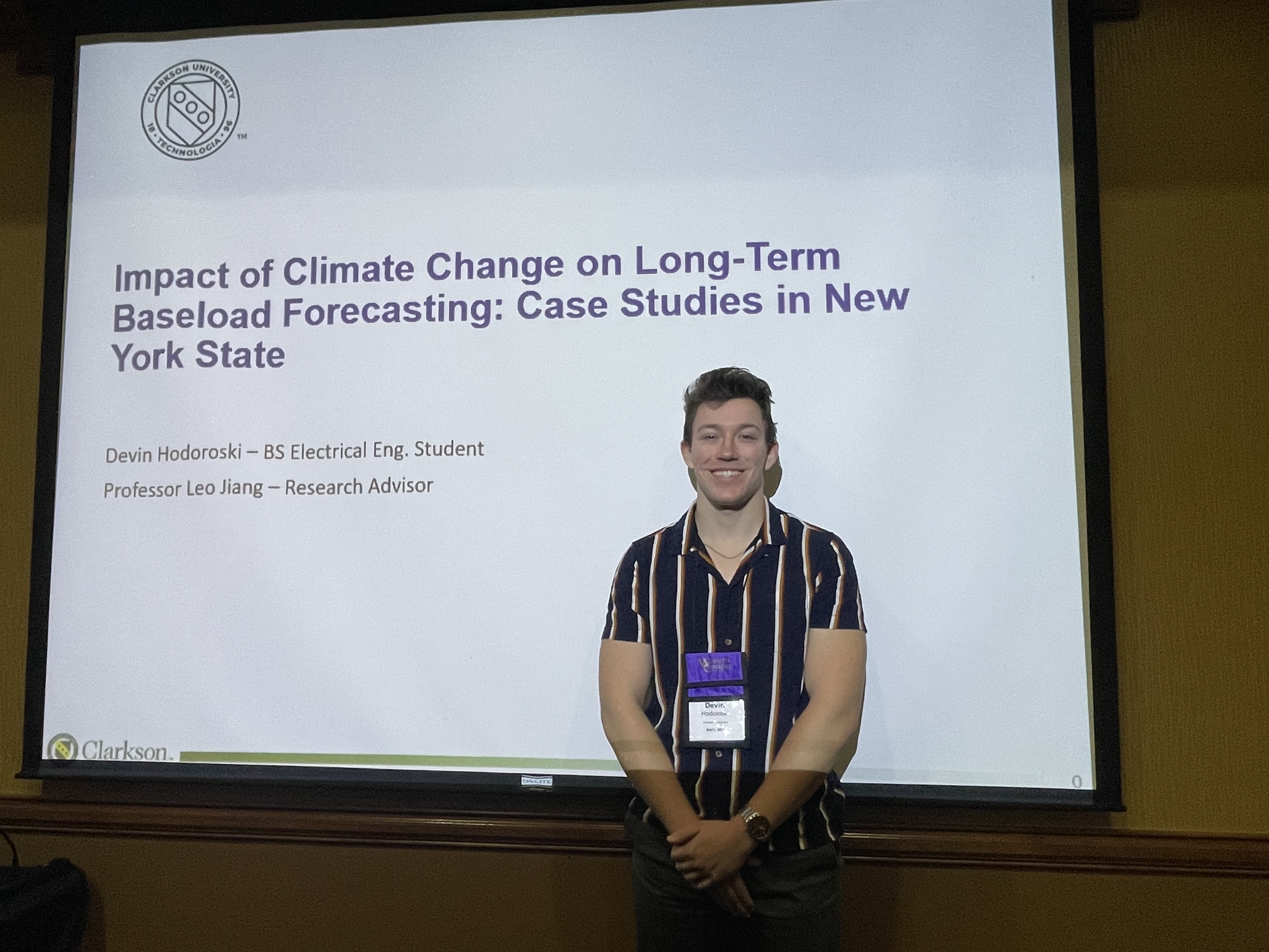 Devin Hodoroski stands in front of the title slide of their presentation at the North American Power Symposium