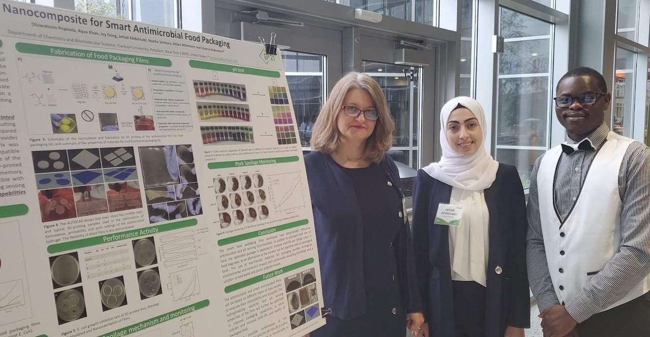 Silvana Andreescu stands with two students presenting a poster on Food Spoilage Mitigation through packaging. 