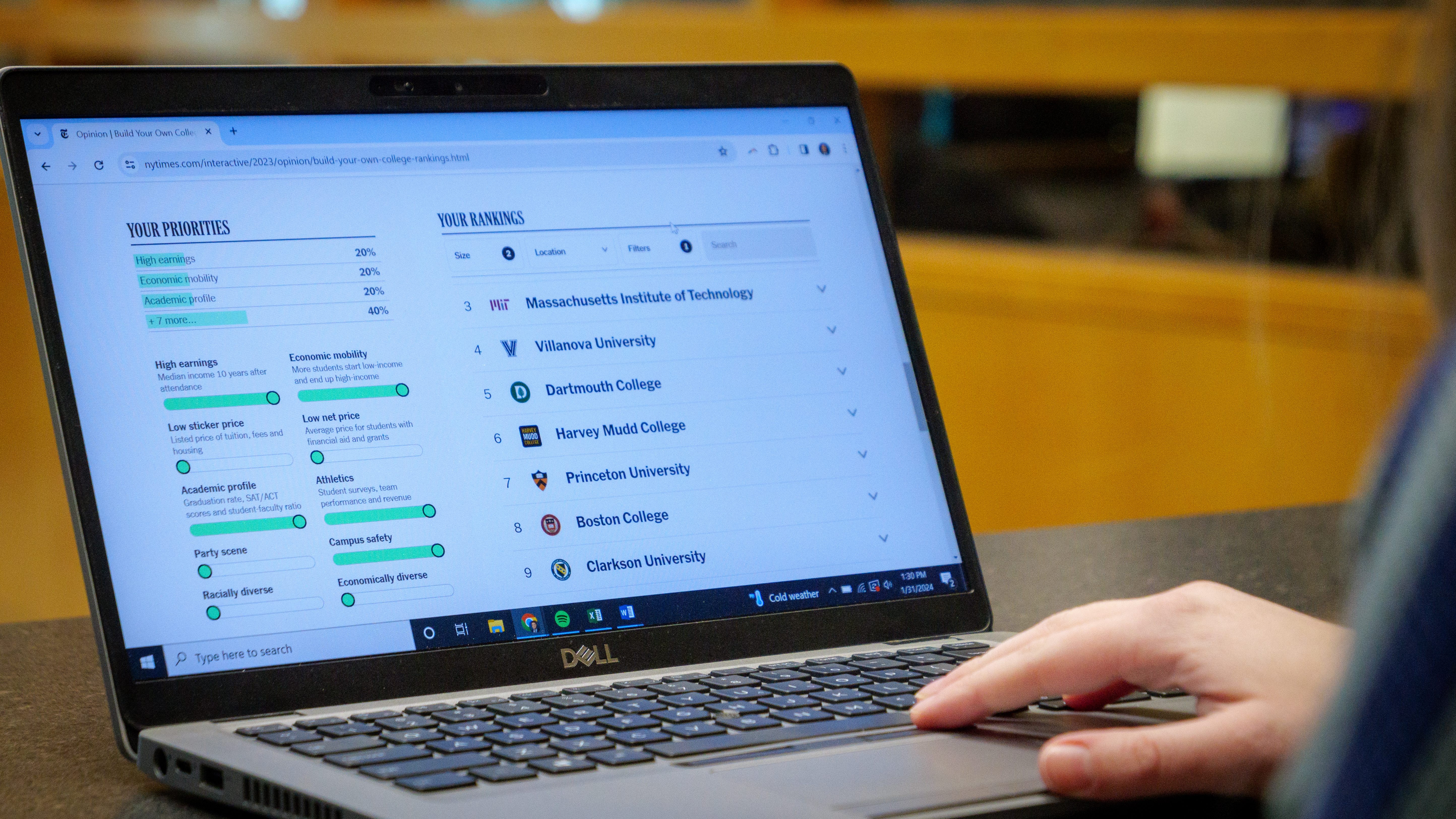 A student’s hand rests on a laptop as the screen shows them exploring the New York Times College Rankings Tool. 