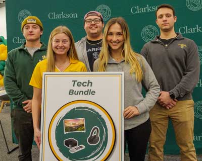 A group of five students poses in front of a green Clarkson University backdrop holding a poster that reads "Tech Bundle."