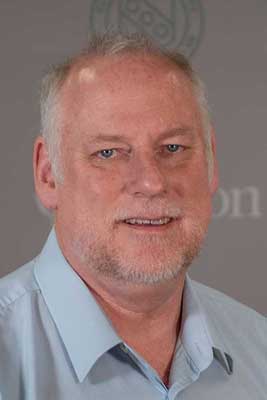 Head shot of John Milne is a blue, open-collared shirt.