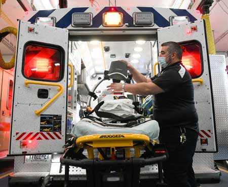 An EMT prepares a medical gurney at the back of an open ambulance.