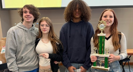 four students pose for a photo with a large trophy