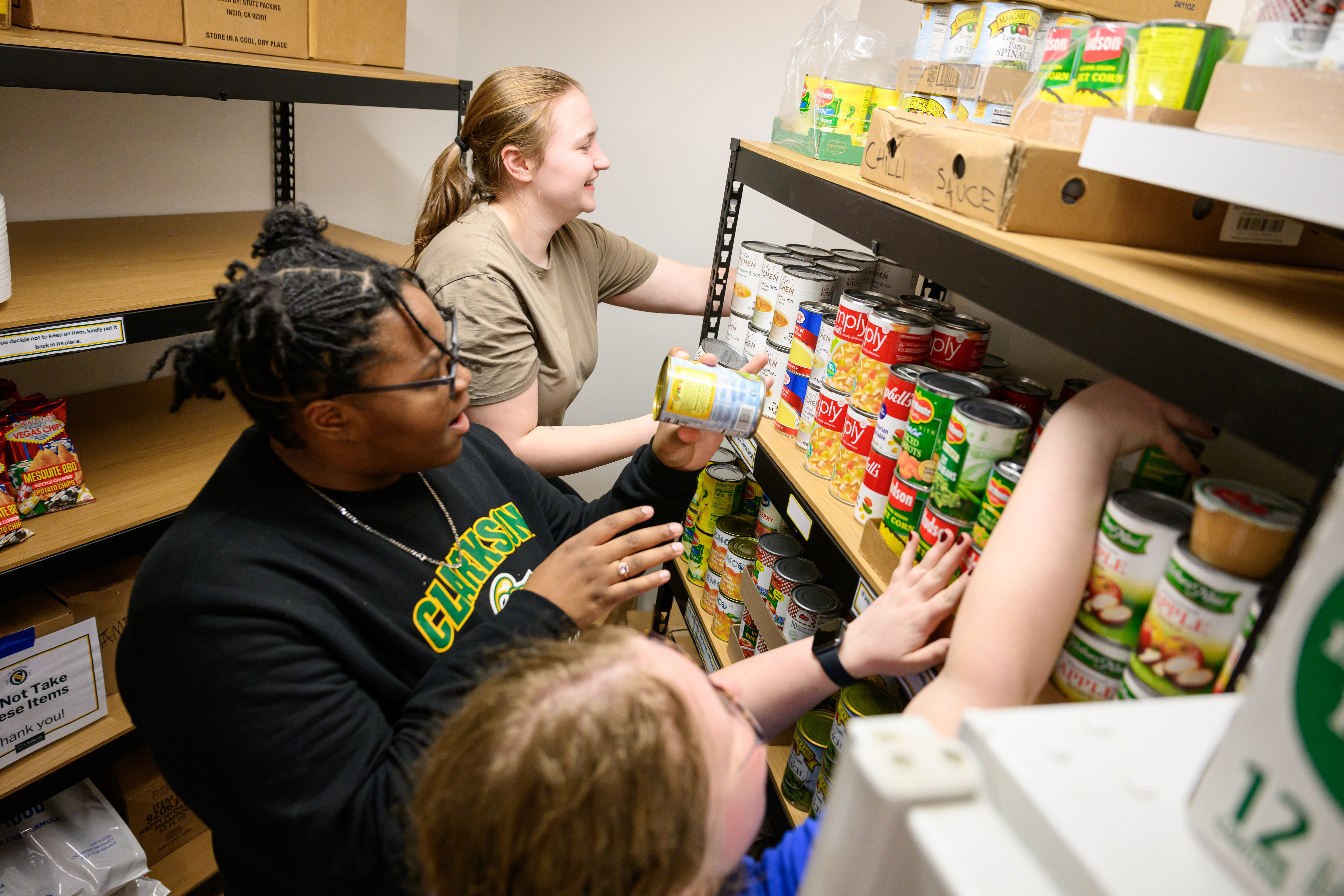 Three students stock pantry shelves with canned food