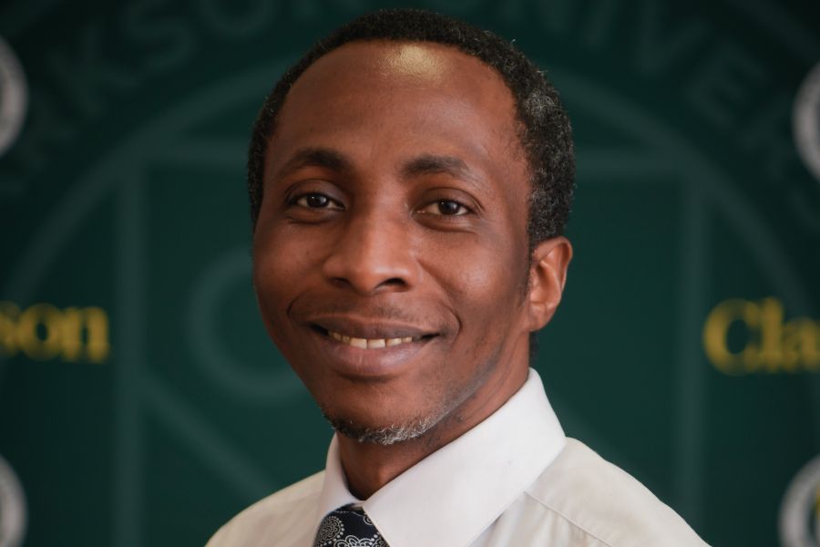 A professional headshot of Professor Kwadwo Appiah-Kubi smiling in front of a green Clarkson University backdrop. He is wearing a white dress shirt and a patterned tie.