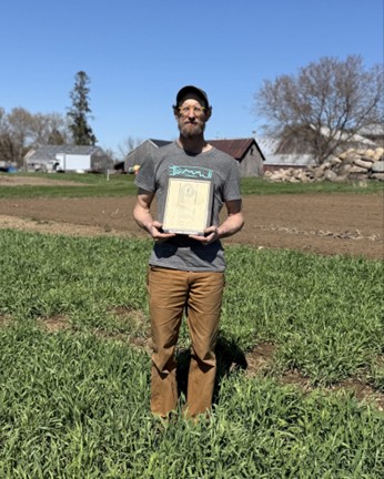 A man stands in an agricultural field holding a certificate