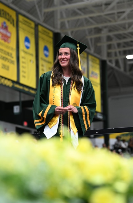A student smiles as she crosses a stage in commencement regalia