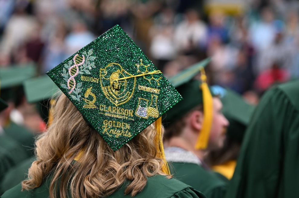 A student's graduation cap adorned with green glitter and sparkly gold lettering, with a double helix