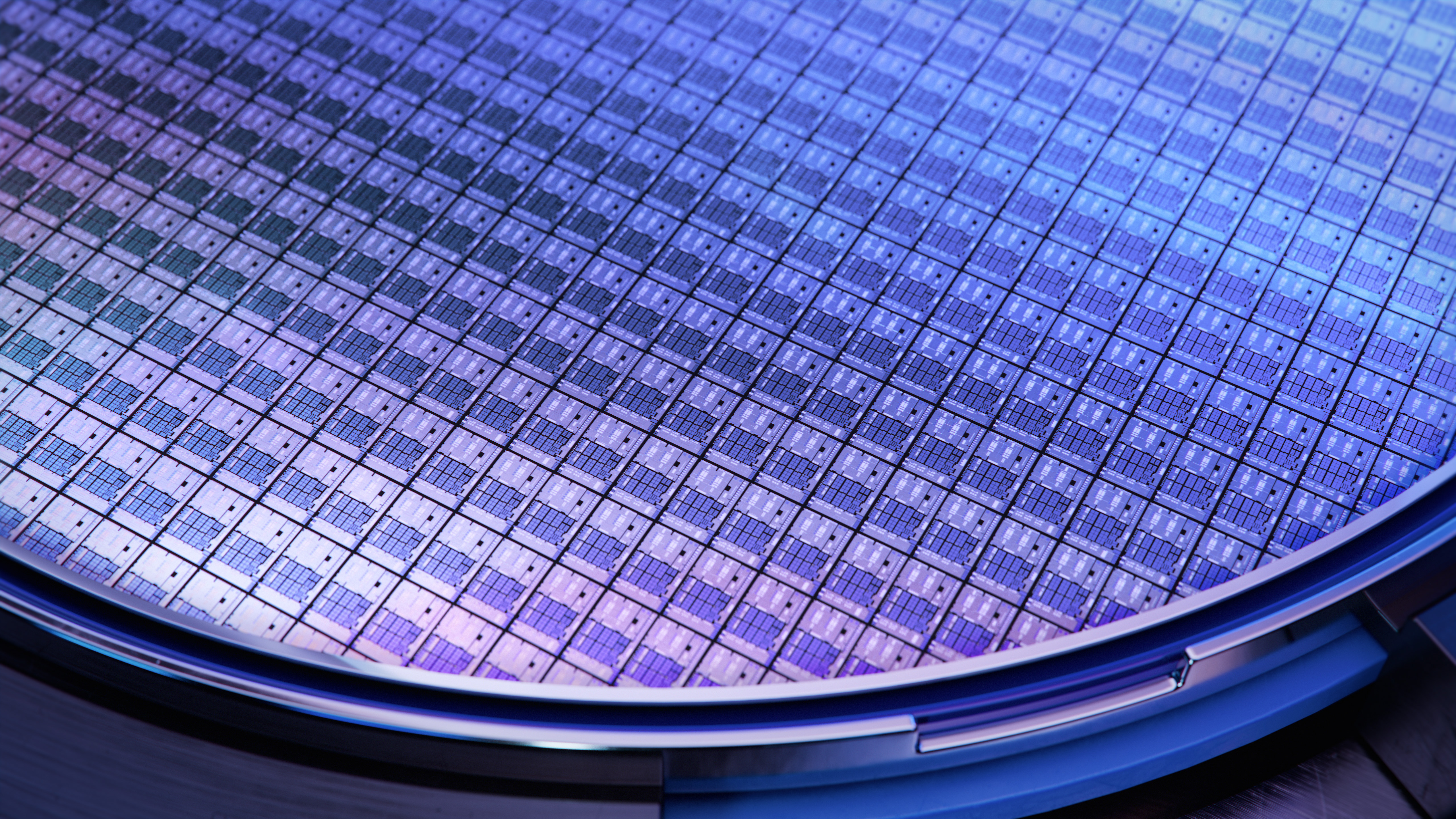Close-up of a silicon semiconductor wafer containing hundreds of square microchips arranged in a precise grid. The wafer reflects blue and purple light, highlighting the intricate patterns used to manufacture advanced electronic, photonic and semiconductor devices.